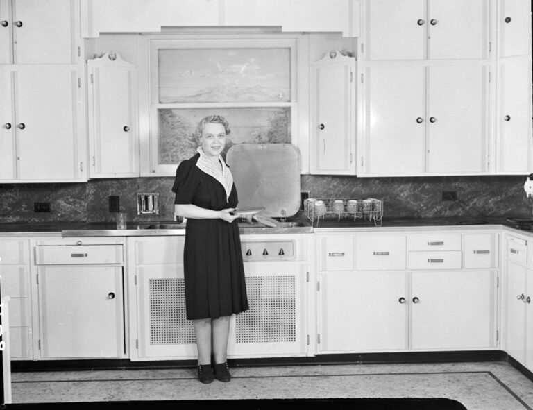 Žena v kuchyni, 1939. Pravděpodobně ukázková kuchyně vzhledem k falešnému pohledu v okně. Pravděpodobně v Seattlu, Washington, vzhledem ke zdroji. Za ní je 