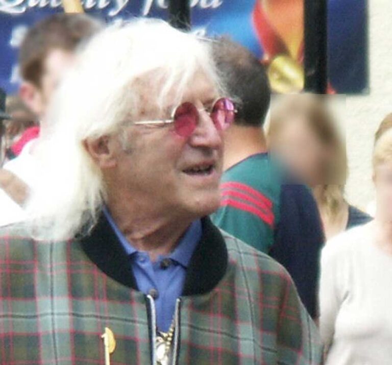 Sir James Alfred Savile OBE (1926-2011), známý spíše jako Jimmy Savile, byl britský televizní moderátor, DJ a filantrop. Během své kariéry se stal populární osobností britské televize, známý pro své excentrické oblečení, hrubý humor a práci s charitativními organizacemi. Foto: Jimmy_Savile_PICT6249a_gaussian_blur.jpg : Původní uživatel, který video nahrál, byl Jmb na anglické Wikipedii. Odvozené dílo: Maximilian Schönherr - Tento soubor byl odvozen od: Jimmy Savile PICT6249a gaussian blur.jpg CC DO 2.5