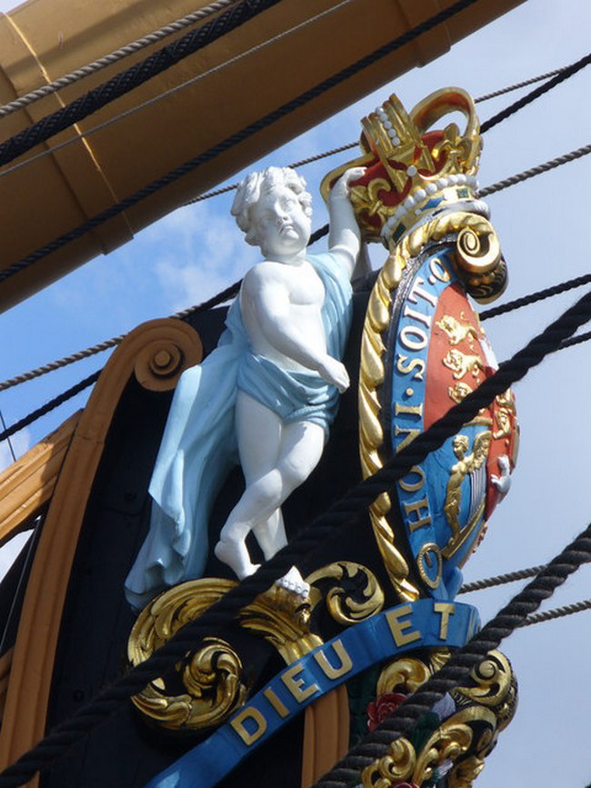 Detail galionové figury: zdobení na přídi tvoří královský znak Spojeného království doplněný postavami putti (cherubínů) a nápisem s mottem britského panovníka „Dieu et mon droit“ (Bůh a mé právo).